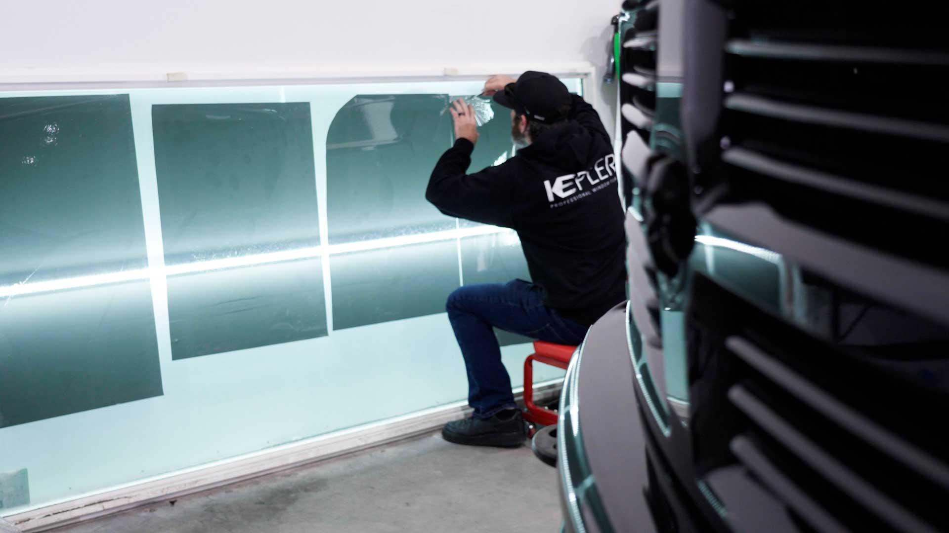 Kepler installer preparing window film panels on a lit workshop wall