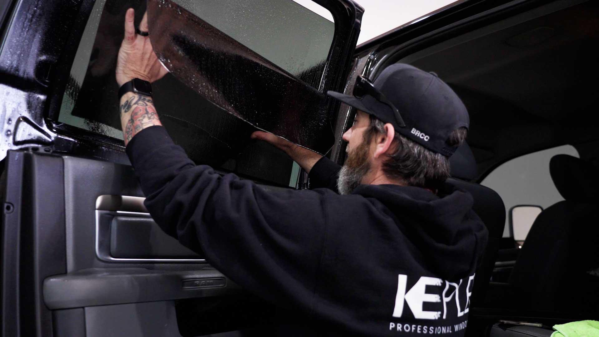 Kepler installer in a cap applying film to a side door window