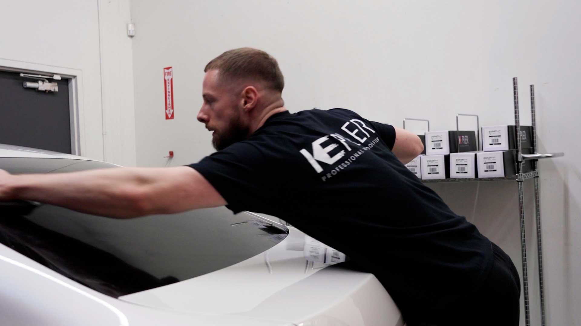 Kepler installer cleaning a rear vehicle window after film installation