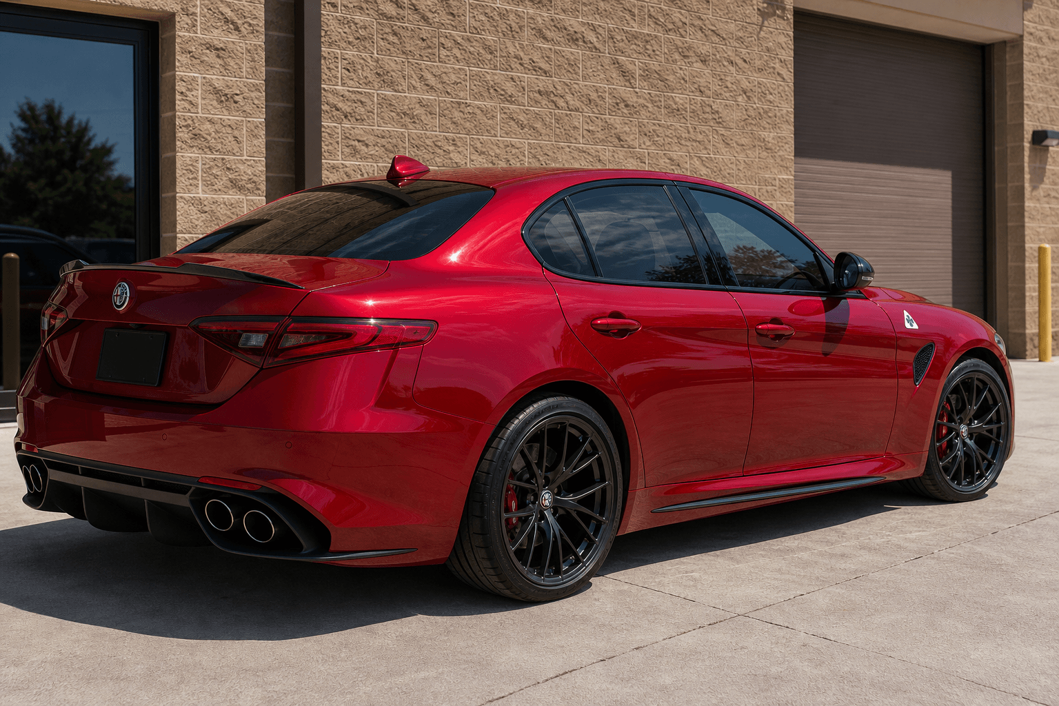 Red Alfa Romeo Giulia-style sedan with dark reflective window tint outside an industrial tint shop